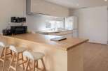 Modern kitchen with light wood countertops and white cabinets, featuring a breakfast bar with three minimalist stools.