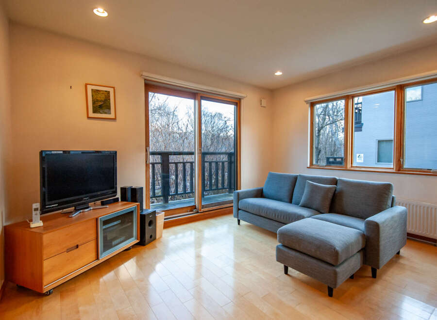 This cozy living room features hardwood floors, large windows offering ample natural light, and a comfortable sectional sofa perfect for relaxation.