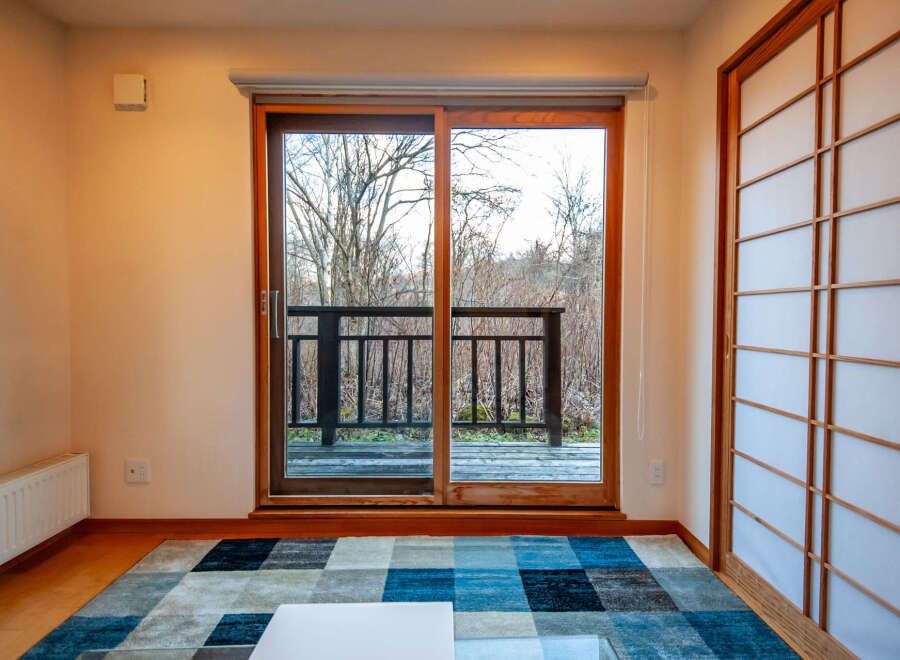 This serene room features a sliding glass door that opens to a deck overlooking a tranquil wooded area, offering a peaceful view.