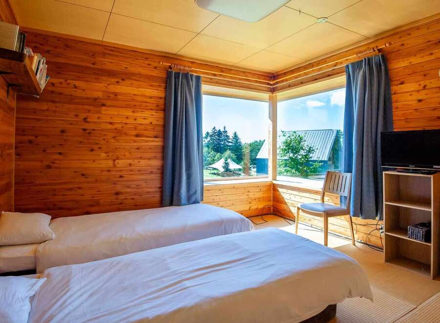Cozy wooden cabin room with two twin beds, a flat-screen TV, and a large window offering scenic views.