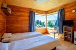 Cozy wooden cabin room with two twin beds, a flat-screen TV, and a large window offering scenic views.