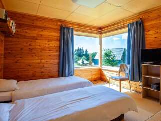 Cozy wooden cabin room with two twin beds, a flat-screen TV, and a large window offering scenic views.
