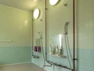 This clean and modern bathroom features two shower stalls with exposed copper pipes, sleek chrome fixtures, and built-in shelves for toiletries.