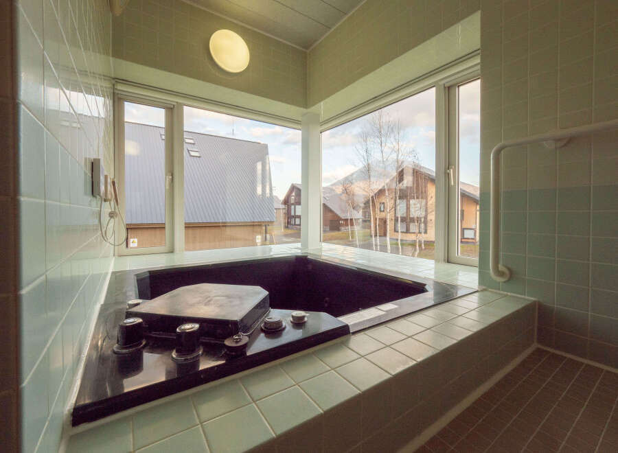 This modern bathroom boasts a built-in hot tub with stunning views of the surrounding landscape, including snow-capped mountains and charming houses.