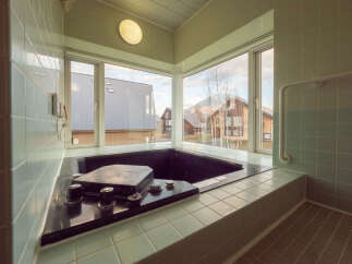 This modern bathroom boasts a built-in hot tub with stunning views of the surrounding landscape, including snow-capped mountains and charming houses.