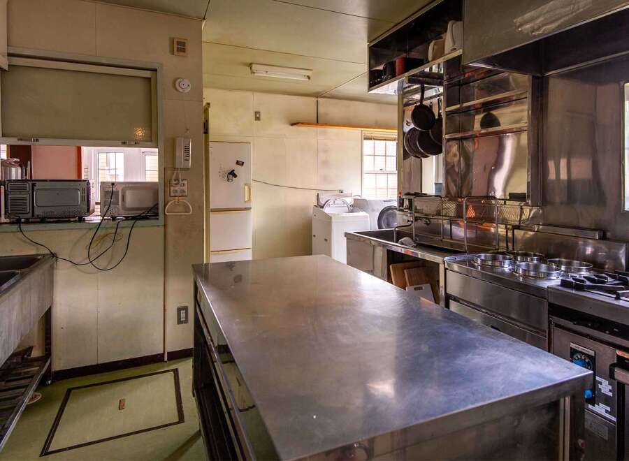 This commercial kitchen boasts ample stainless steel counter space, a large sink, and a full suite of appliances including a stovetop, oven, and microwave.
