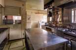 This commercial kitchen boasts ample stainless steel counter space, a large sink, and a full suite of appliances including a stovetop, oven, and microwave.