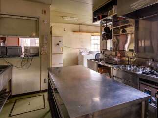 This commercial kitchen boasts ample stainless steel counter space, a large sink, and a full suite of appliances including a stovetop, oven, and microwave.