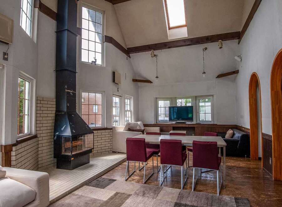 This spacious living area features a stunning high ceiling with exposed beams, large windows offering ample natural light, and a cozy fireplace as a focal point.