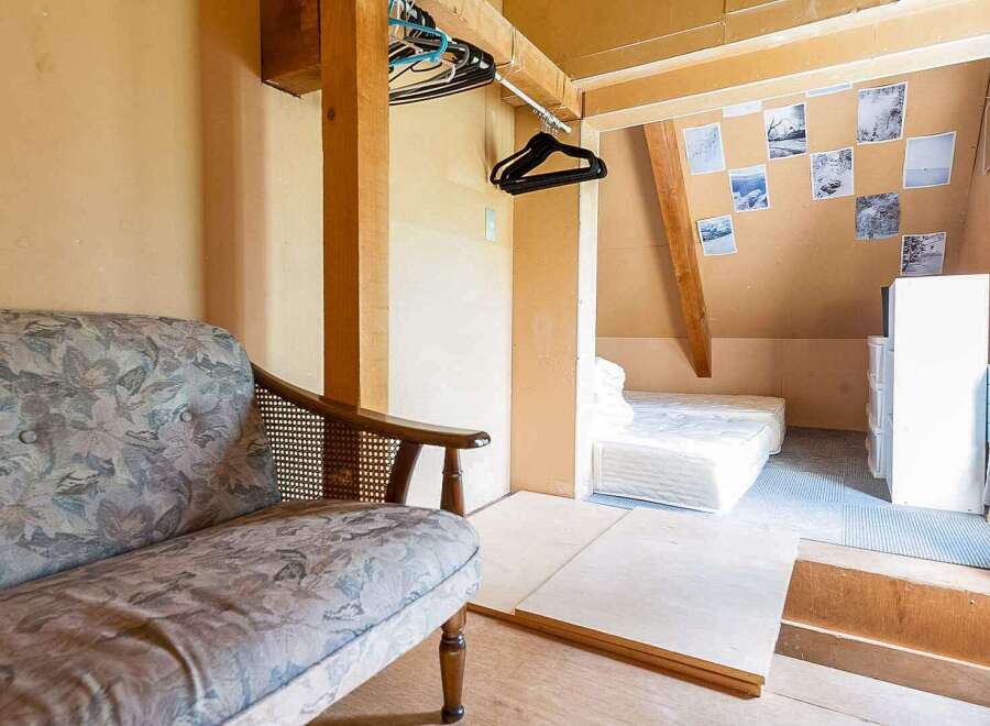 Cozy attic room with a floral patterned couch, wooden closet, and a built-in bed.