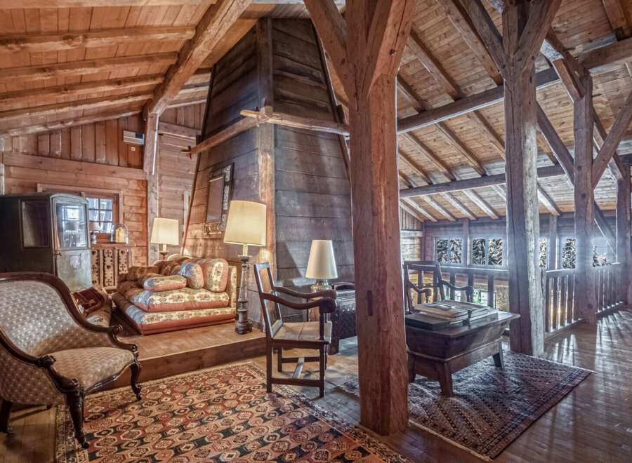 Rustic charm meets modern comfort in this unique chalet featuring exposed wooden beams, a cozy sitting area with antique furniture, and a stunning stone fireplace.