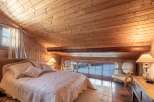Cozy chalet bedroom with wooden walls and ceiling, featuring a comfortable queen-size bed and large windows offering stunning views.
