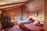 Cozy chalet bedroom with twin beds, wooden walls and ceiling, and views of snowy trees.