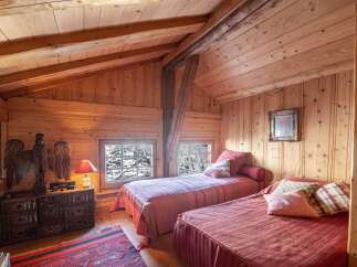 Cozy chalet bedroom with twin beds, wooden walls and ceiling, and views of snowy trees.