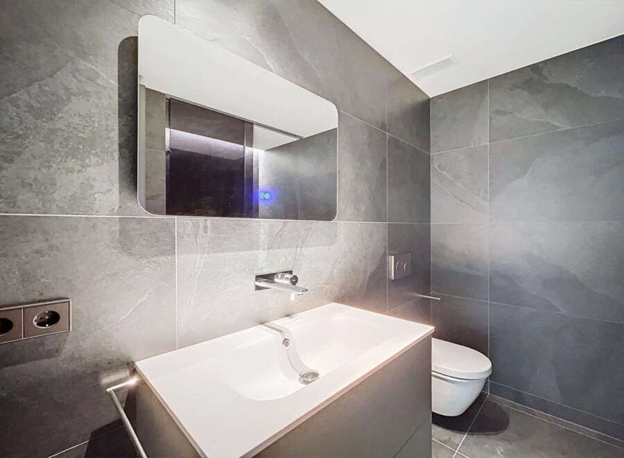 Modern bathroom with sleek gray tile, floating vanity, and frameless mirror.