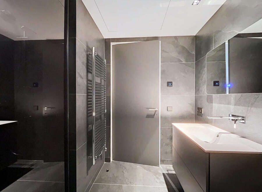 Modern bathroom with dark gray tiles, sleek fixtures, and a frameless glass shower enclosure.