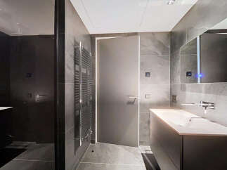 Modern bathroom with dark gray tiles, sleek fixtures, and a frameless glass shower enclosure.