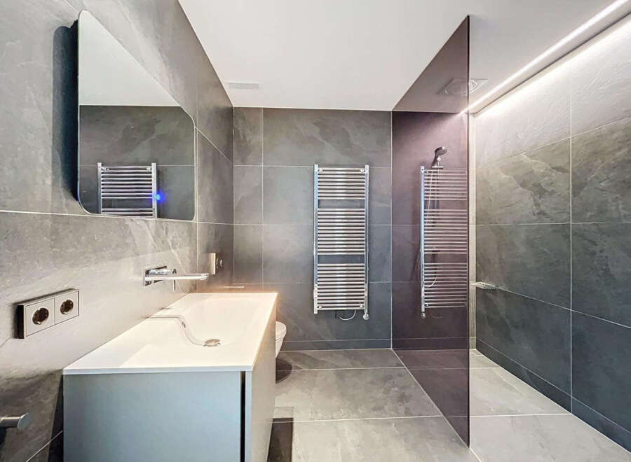 Modern bathroom with sleek gray tile, frameless shower, and contemporary fixtures.