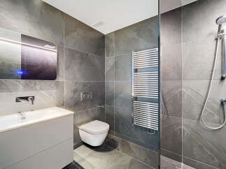 Modern bathroom with sleek gray tile, a floating vanity, and a frameless glass shower enclosure.
