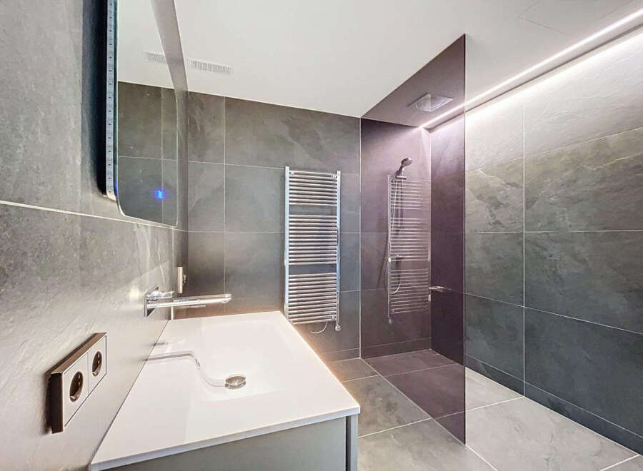 Modern bathroom with sleek gray tile, frameless glass shower, and floating vanity.