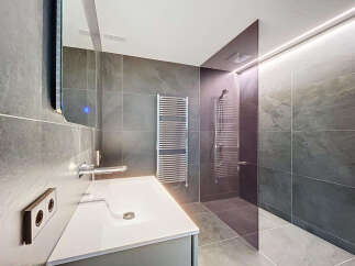Modern bathroom with sleek gray tile, frameless glass shower, and floating vanity.