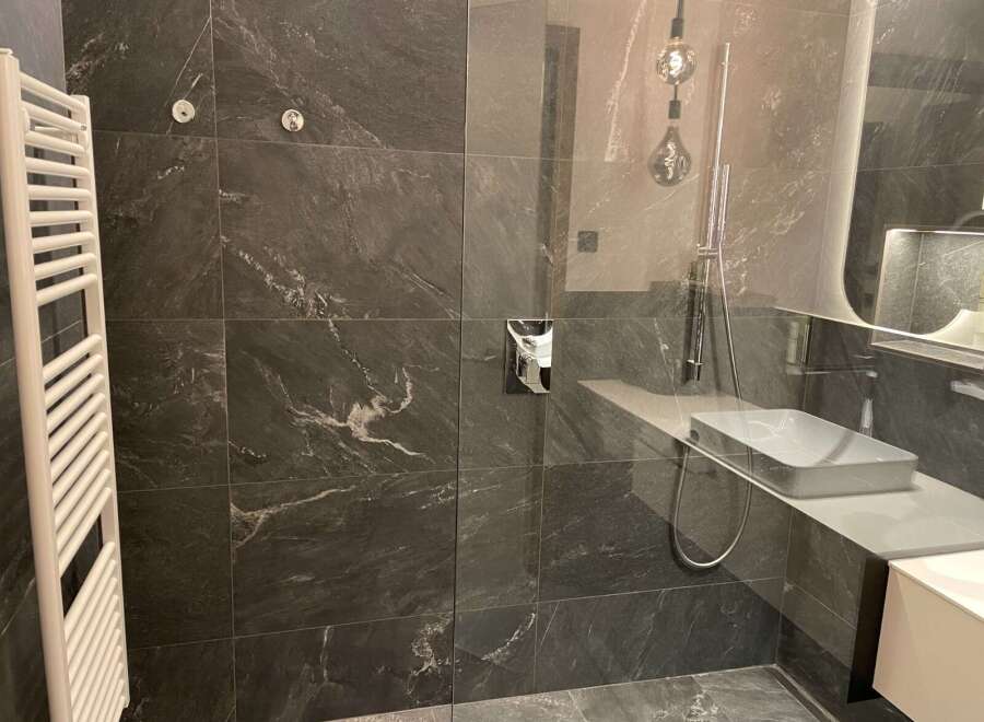 Step into luxury with this stunning bathroom featuring sleek, dark tile and modern fixtures.