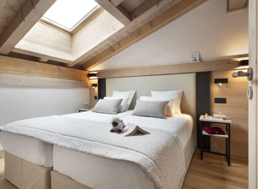 Cozy attic bedroom with wooden beams and skylights, featuring a double bed with plush bedding and a sheep toy.