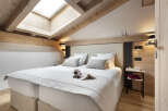 Cozy attic bedroom with wooden beams and skylights, featuring a double bed with plush bedding and a sheep toy.