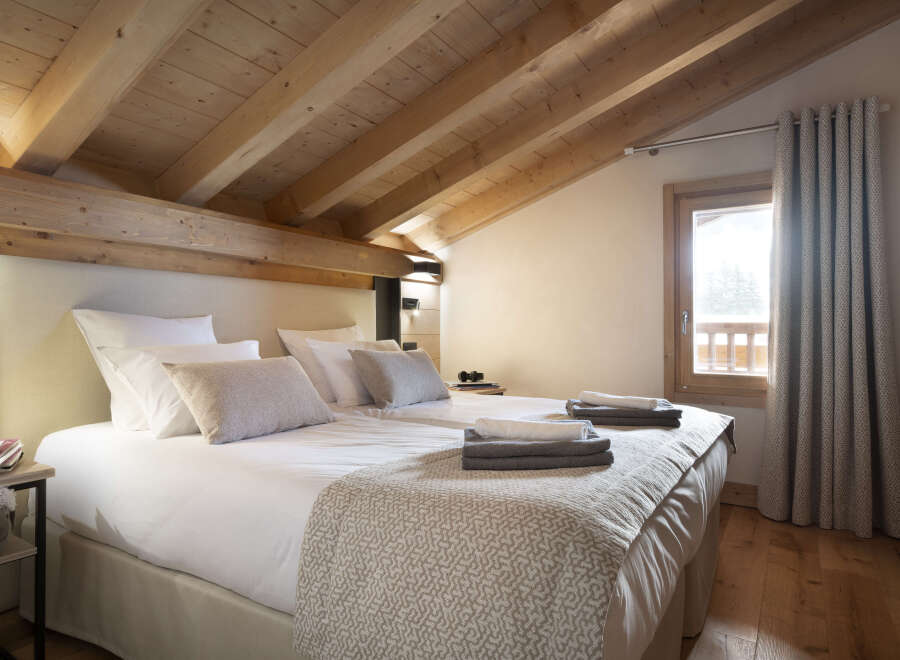 Cozy chalet bedroom with wooden beams, plush bedding, and a view of the snowy landscape.