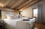 Cozy chalet bedroom with wooden beams, plush bedding, and a view of the snowy landscape.