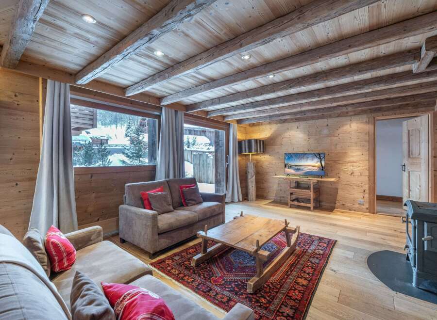 Cozy chalet living room with exposed wooden beams, a stunning mountain view, and a warm wood-burning stove.