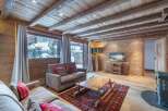 Cozy chalet living room with exposed wooden beams, a stunning mountain view, and a warm wood-burning stove.