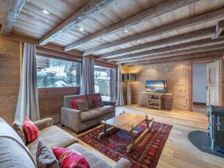 Cozy chalet living room with exposed wooden beams, a stunning mountain view, and a warm wood-burning stove.