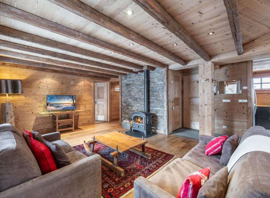 Cozy chalet living room with exposed wooden beams, stone fireplace, and plush sofas.