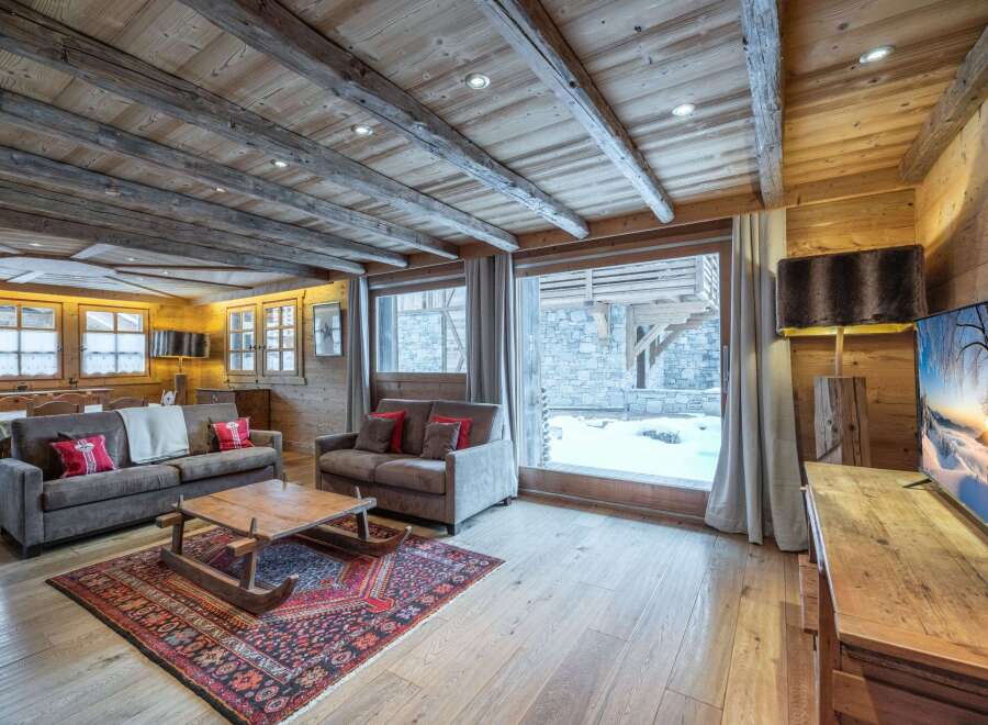 This stunning chalet boasts a spacious living area with exposed wooden beams and a cozy fireplace, creating a warm and inviting atmosphere.