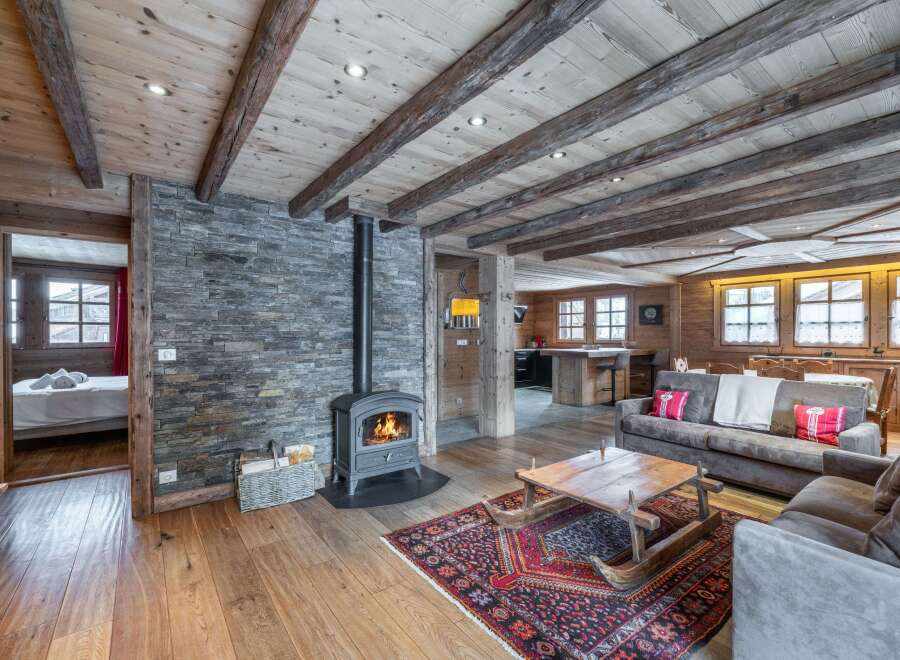 This stunning chalet boasts a cozy living room with a wood-burning stove, exposed wooden beams, and a stone feature wall.