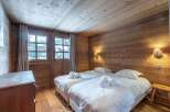 Cozy chalet bedroom with twin beds, wooden walls and ceiling, and a view of the snowy landscape.