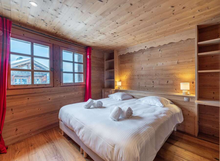 Cozy chalet bedroom with wooden walls and ceiling, featuring a comfortable double bed and crisp white linens.