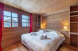 Cozy chalet bedroom with wooden walls and ceiling, featuring a comfortable double bed and crisp white linens.