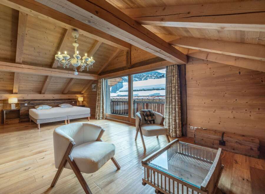 This stunning chalet boasts a spacious bedroom with a king-size bed, exposed wooden beams, and large windows offering breathtaking views of the snowy mountains.