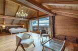 This stunning chalet boasts a spacious bedroom with a king-size bed, exposed wooden beams, and large windows offering breathtaking views of the snowy mountains.