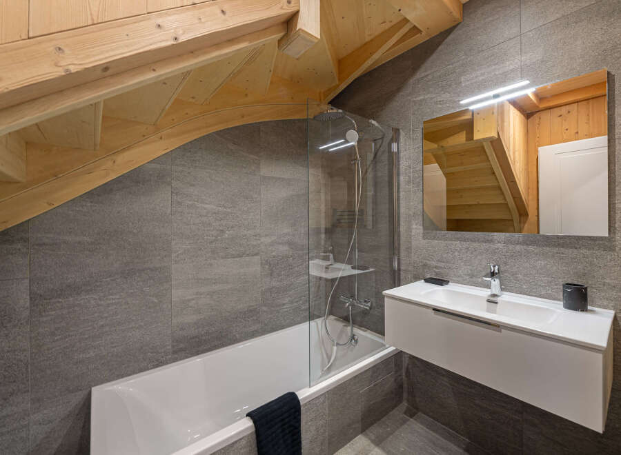 This stunning bathroom boasts a modern design with gray tile, a sleek white vanity, and a glass-enclosed bathtub.