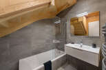 This stunning bathroom boasts a modern design with gray tile, a sleek white vanity, and a glass-enclosed bathtub.