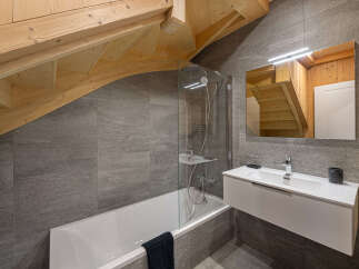 This stunning bathroom boasts a modern design with gray tile, a sleek white vanity, and a glass-enclosed bathtub.