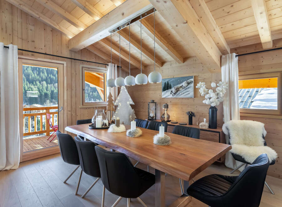 This stunning chalet boasts a spacious dining area with a live-edge wooden table, perfect for enjoying meals with breathtaking mountain views.