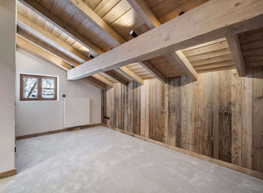 This stunning attic conversion boasts exposed wooden beams and reclaimed wood paneling, creating a rustic-chic atmosphere.
