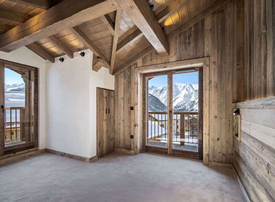 This stunning chalet boasts a spacious bedroom with floor-to-ceiling windows offering breathtaking mountain views.
