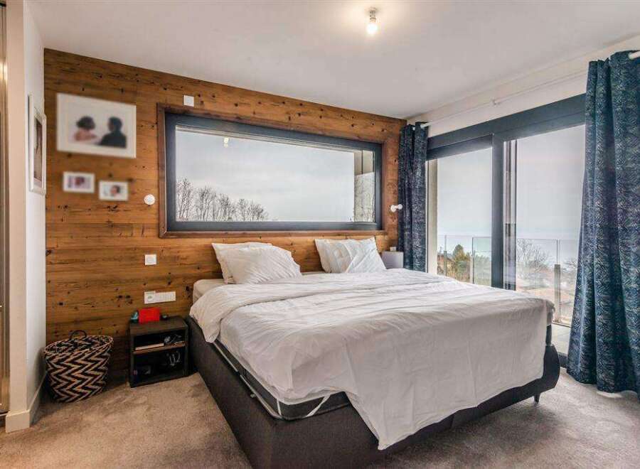 Wake up to breathtaking views from this luxurious bedroom, featuring a stunning wall of windows and a cozy wooden accent wall.