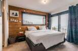 Wake up to breathtaking views from this luxurious bedroom, featuring a stunning wall of windows and a cozy wooden accent wall.