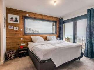 Wake up to breathtaking views from this luxurious bedroom, featuring a stunning wall of windows and a cozy wooden accent wall.